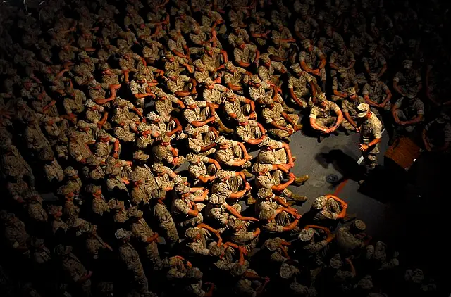 عکس از نمای بالا از تعدادی از تفندگداران دریایی آمریکا که نشته اند و به سخنرانی فرمانده خود که مقابل آنها ایستاده گوش می دهند