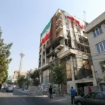 نمای دور از تهران که برج میلاد دیده می شود. در نمای نزدیکتر یک سمت ساختمان بلند تخریب شده و از سمت دیگر پرجم جمهوری اسلامی در ابعاد بزرگ نصب شده است