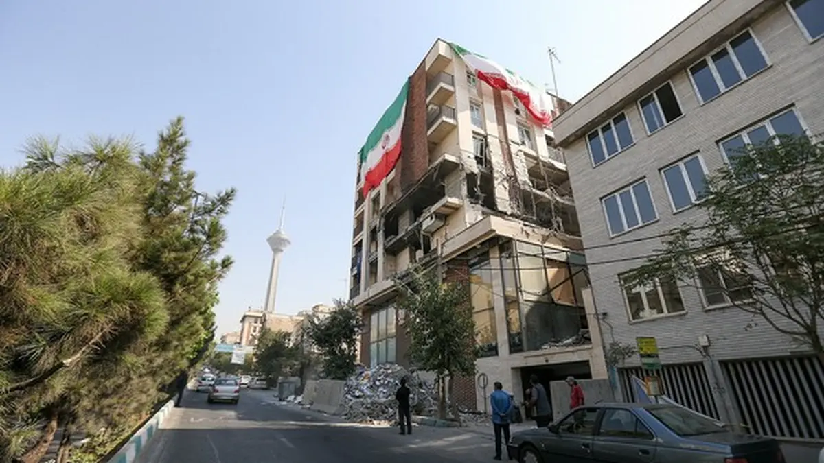 نمای دور از تهران که برج میلاد دیده می شود. در نمای نزدیکتر یک سمت ساختمان بلند تخریب شده و از سمت دیگر پرجم جمهوری اسلامی در ابعاد بزرگ نصب شده است
