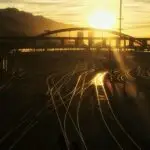 تصویر غروب که روی پل بزرگ و ریل های راه آهن و کوه سایه انداخته است.