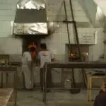 دو نانوا در حال پخت نان سنگک و یک پیرمرد مشتری دورتر از آنها نشسته است و منتظر است