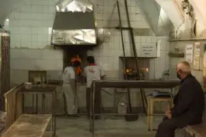 دو نانوا در حال پخت نان سنگک و یک پیرمرد مشتری دورتر از آنها نشسته است و منتظر است