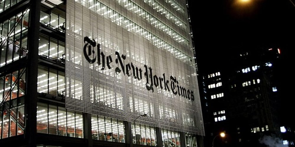 ساختمان شیشیه ای نیویورک تایمز در شب با چزاغ های روشن. روی ساختمان به انگلیسی نوشته شده است نیویورک تایمز
