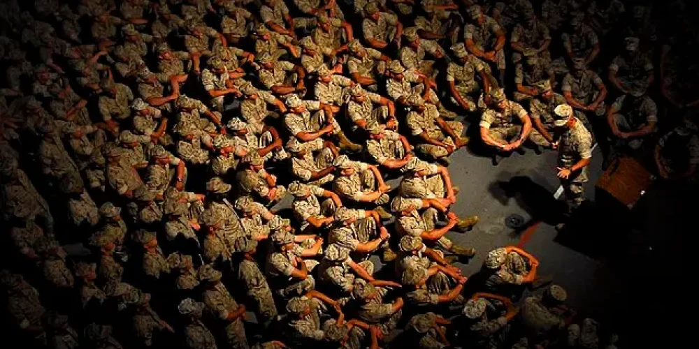 عکس از نمای بالا از تعدادی از تفندگداران دریایی آمریکا که نشته اند و به سخنرانی فرمانده خود که مقابل آنها ایستاده گوش می دهند