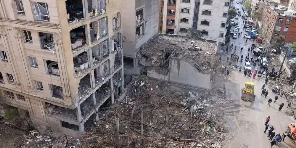 از نمای بالا یک آپارتمان در حمله هوایی در تهران تخریب شده و ساختمان های اطراف هم آسیب دیده. در خیابان هم تعداد زیادی از مردم هستند