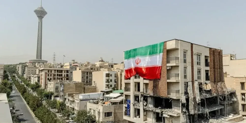 نمای دور از تهران که برج میلاد دیده می شود. در نمای نزدیکتر یک سمت ساختمان بلند تخریب شده و از سمت دیگر پرجم جمهوری اسلامی در ابعاد بزرگ نصب شده است