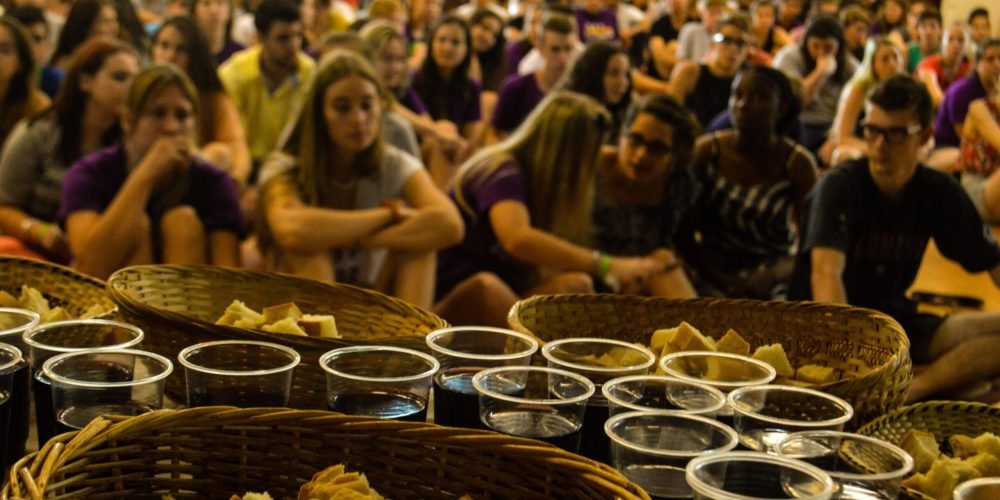 تعداد زیادی زن و مرد نشسته اند و آماده اند تا مراسم نان و شراب مقدس بخورند