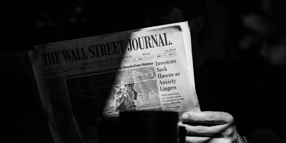 عکس سیاه‌وسفید از فردی که روزنامه وال استریت ژورنال را در دست دارد. تصویر شخص مشخص نیست